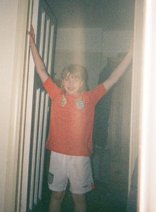 Sports journalist Nancy Gillen as a child wearing an England football kit - red top and white shorts - with her hands in the air.