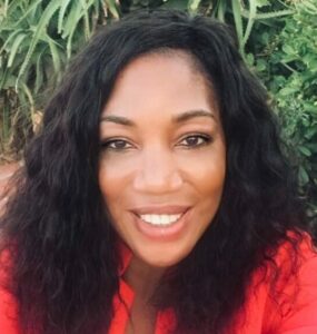 Nichola Ibe is a Black woman with shoulder length hair and wearing a red shirt. She smiles at the camera. 